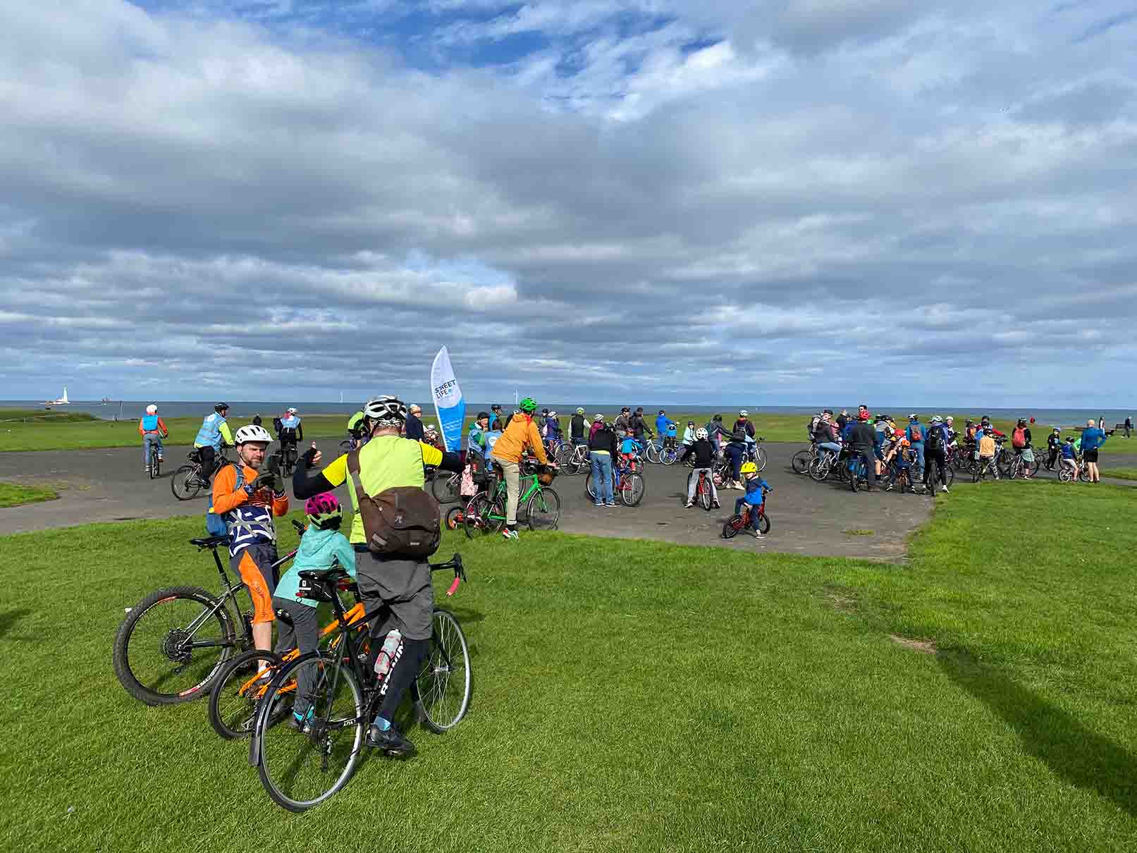 Photo showing riders gathered on The Links in Whitley Bay where we wait for additional riders to join us en-route.  Pictured are riders of all ages and abilities including Street Life ride marshals.